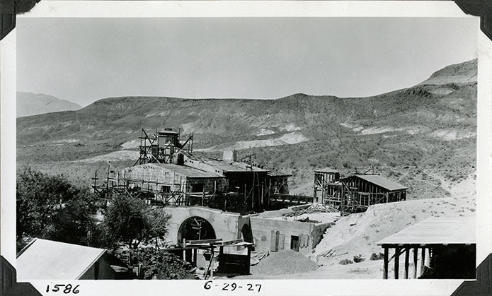 This is an historic black and white photograph from the Scotty's Castle Historic Photograph Collection, Death Valley National Park of Scotty's Castle Main House and Annex, looking southwest. Great Hall fireplace and Kitchen chimney stacks covered. Spanish Bedroom roof tiled. Italian Room fireplace chimney in place. June 29, 1927. Photographed by Mat Roy Thompson.