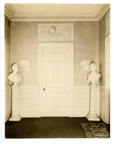 Black and white photograph of a door with three busts and a profile insert above the door.