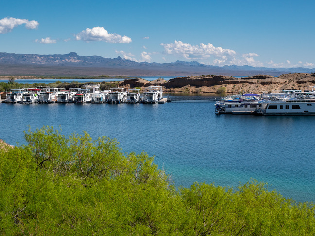 dense foliage foreground, houseboats body of water mid ground, mountains in distance