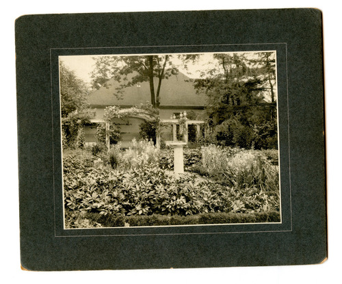 Black and white photograph of formal garden with pedestal and arbor.