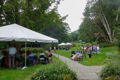 fiddle orchestra performs under pop up tent with a group of onlookers and canopy event tents in background