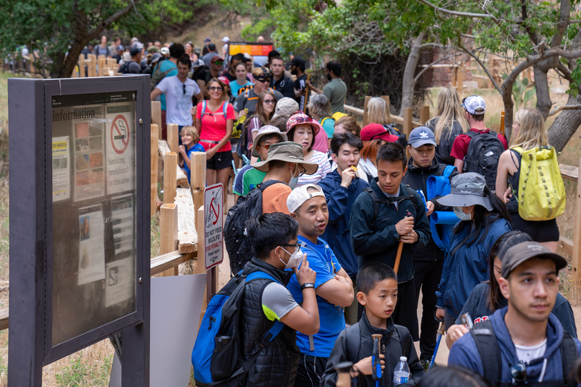 Long line of visitors waits to board park shuttle at Temple of Sinawava shuttle stop in Zion Canyon.