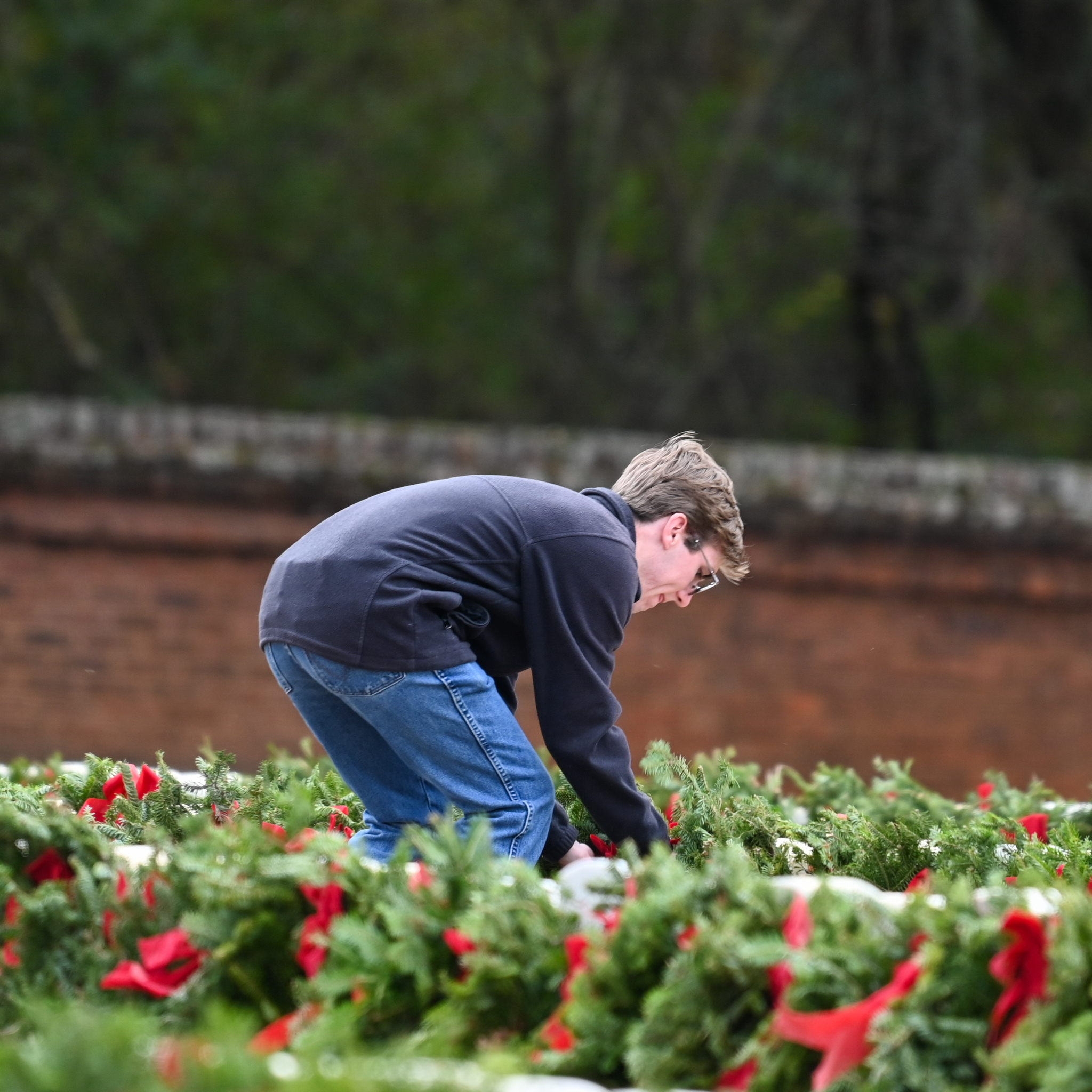 Young man placing a wreath in front of a headstone.