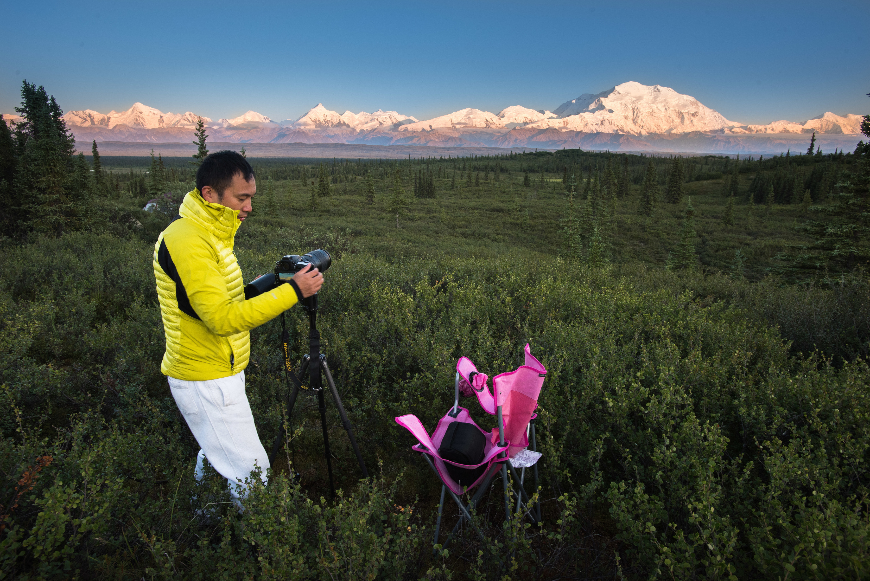 man with camera on a tripod taking photos of snowy mountains