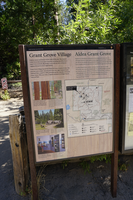 A metal panel with information about Grant Grove sits in a metal frame. Behind it is a wooden fence and trees. 