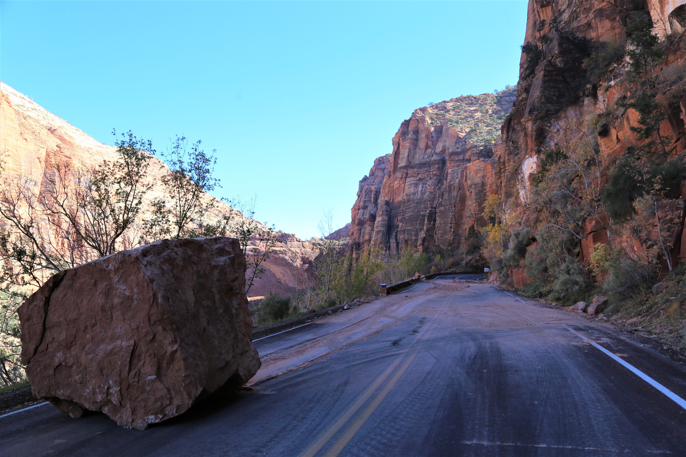 A large boulder sitting on the left lane of SR 9, with the cliffs of Zion in the background