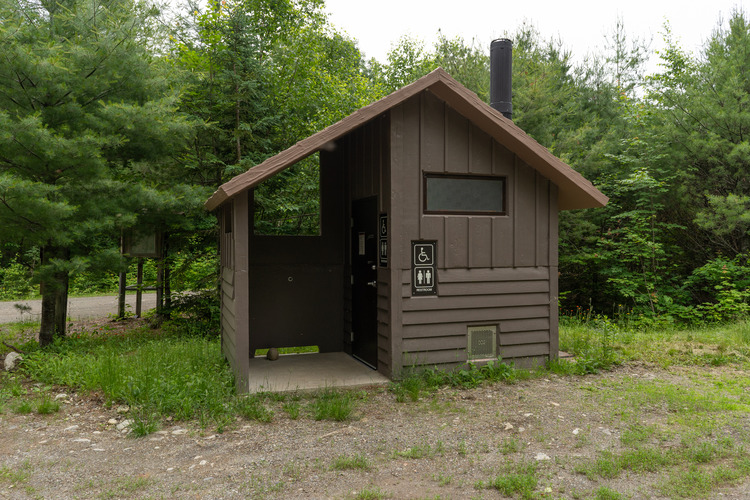 A large brown out house / toilet facility in the woods.