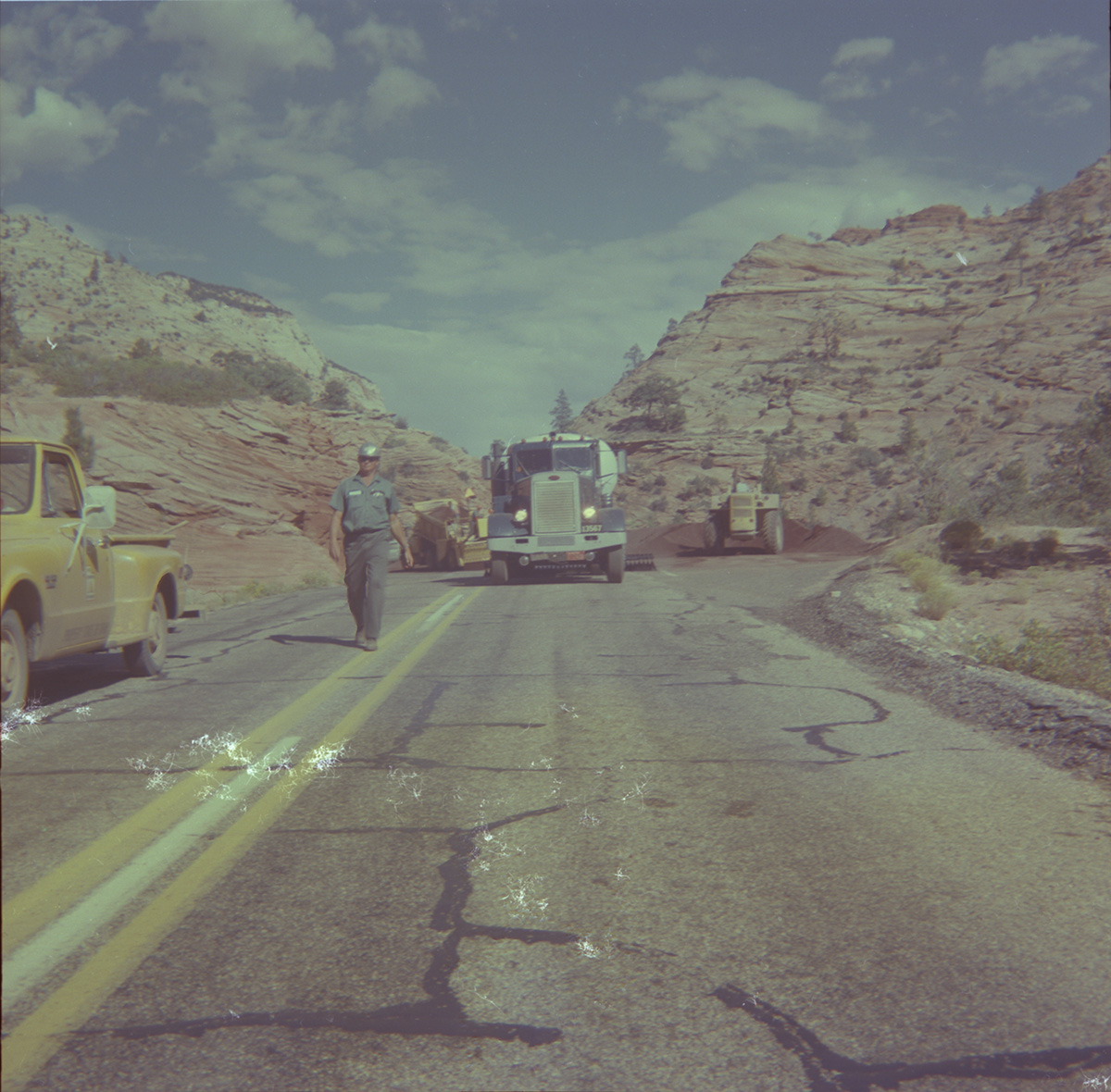 Construction vehicles performing chipsealing operations on the roads of Zion and man worker walking down the street.