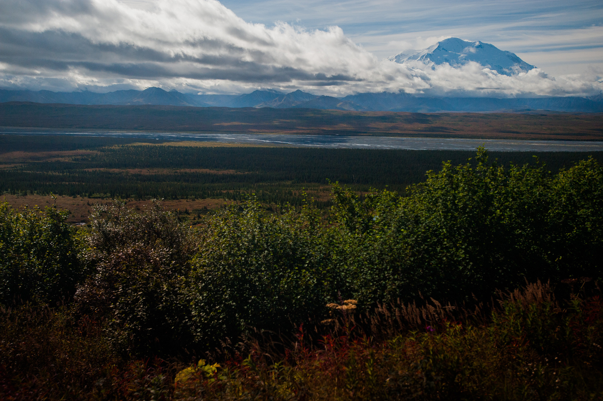 clouds over mountains, with one particularly large peak poking up above the clouds, in front of a landscape of hills and rivers