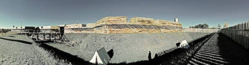A view of the corner of the log fort. Shadows of the fence surrounding stretch into view like dark fingers.