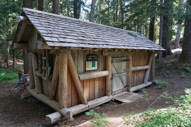 A small cabin with plank siding framed by logs and wood shingle roof. 