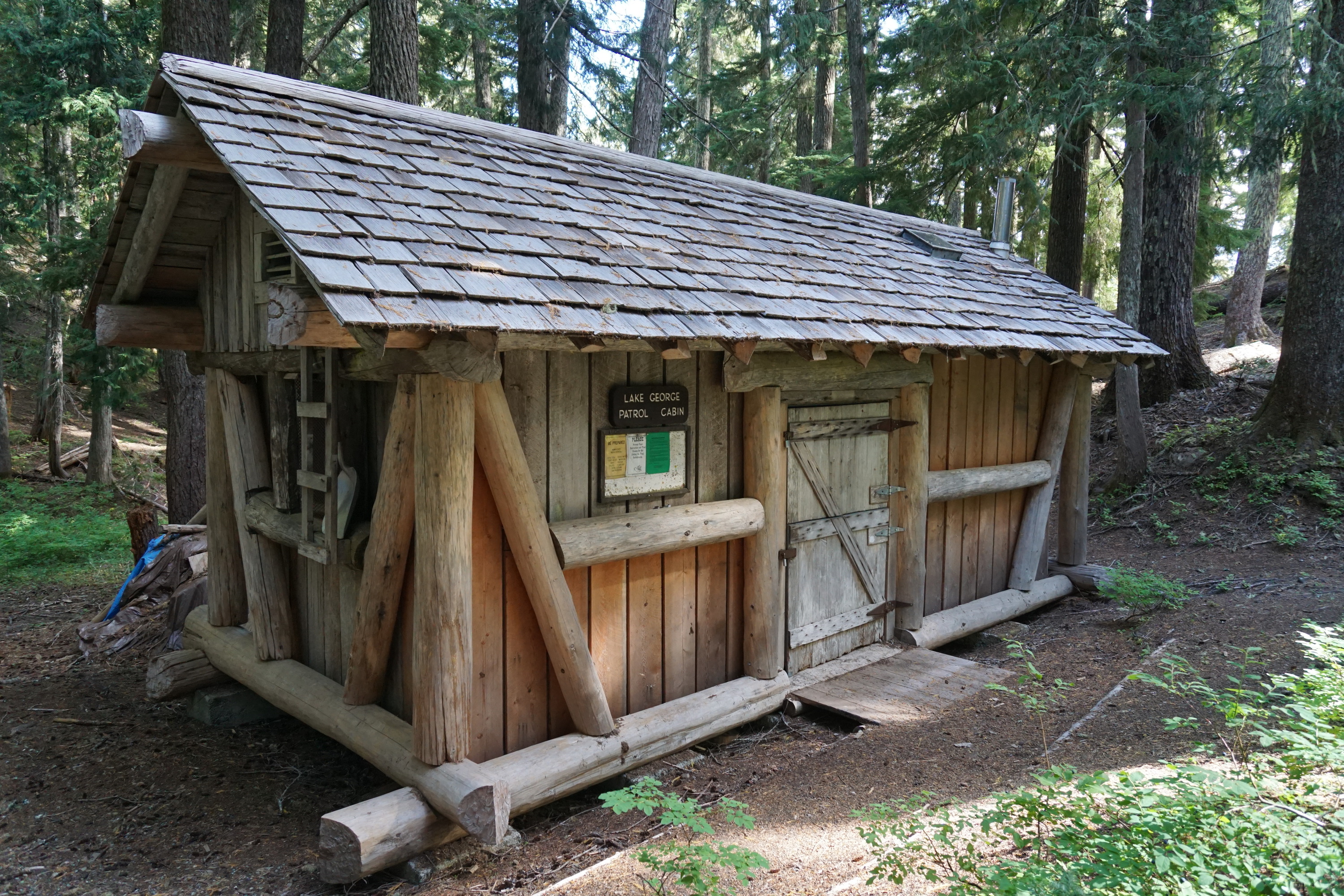 A small cabin with plank siding framed by logs and wood shingle roof. 