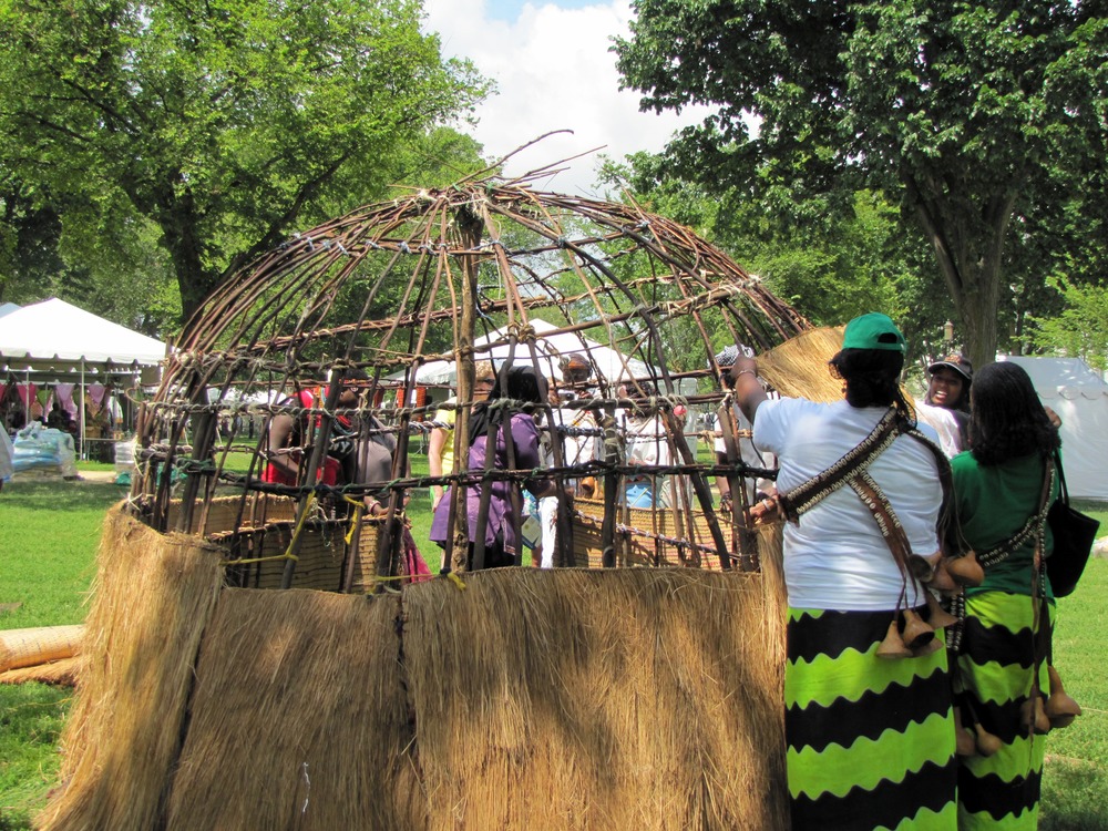 wood frame is having grass woven onto it by people in traditional dress