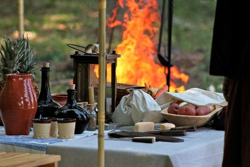 a fire in the background with period cups, bowls and food in the foreground.
