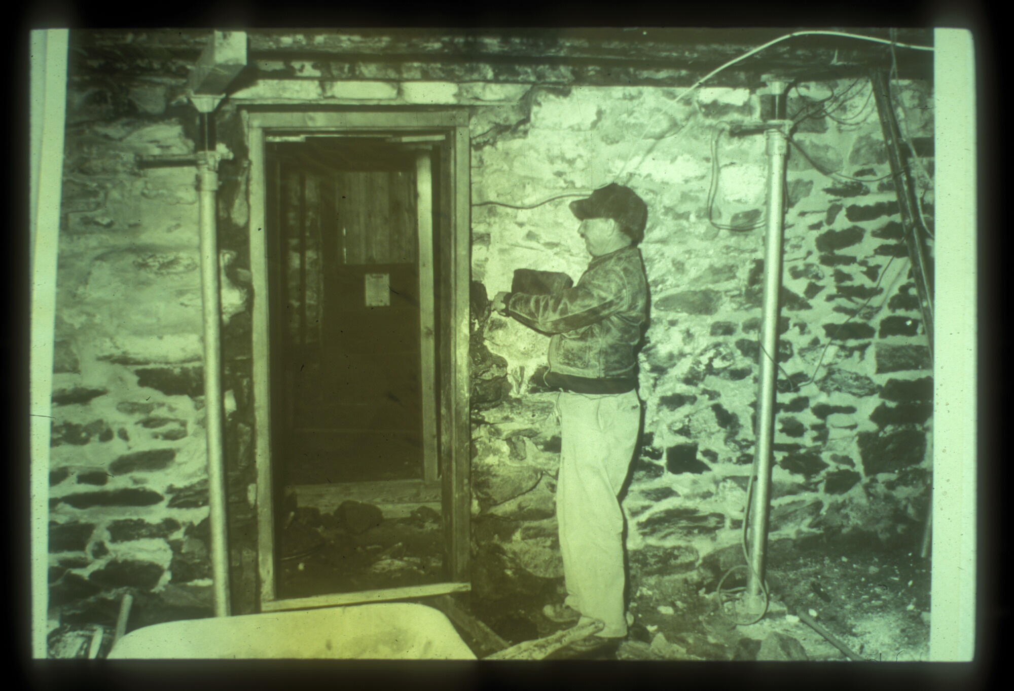 A man stands beside a narrow doorway in a stone wall