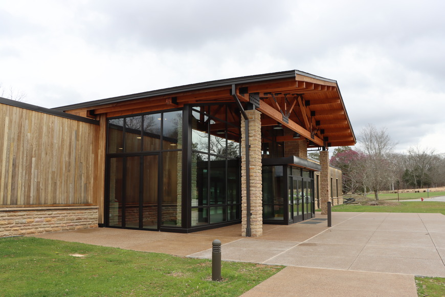 A large wooden framed building with stone columns and large glass windows with black metal framing.