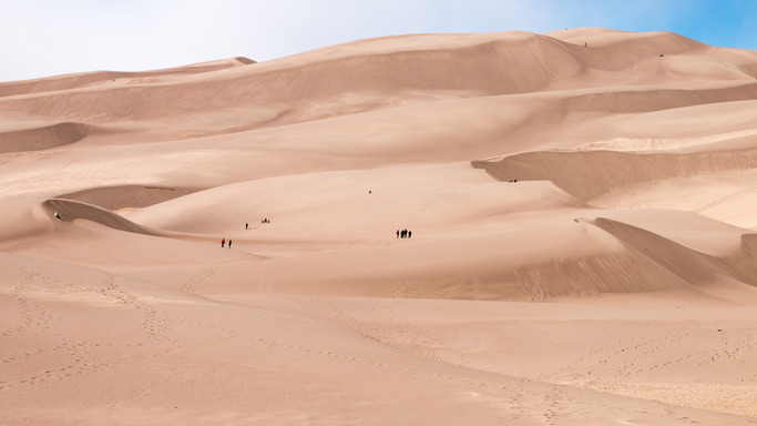 Visitors walk on and climb up large sand dunes. 