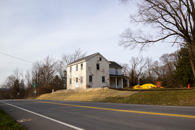 Zoomed out view of a white brick home sitting on a hill with a road in front. 