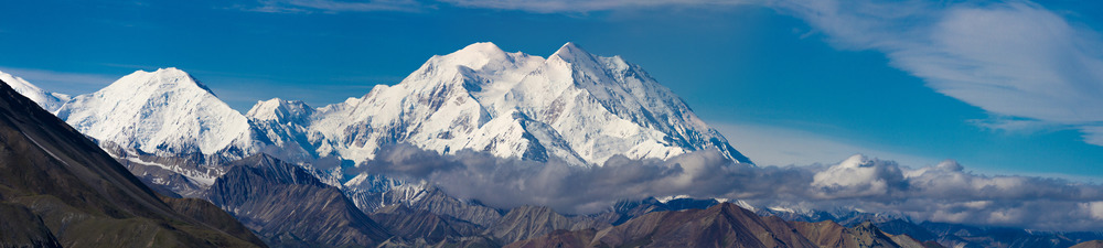 A landscape of hills, forests and a huge, snowy mountain