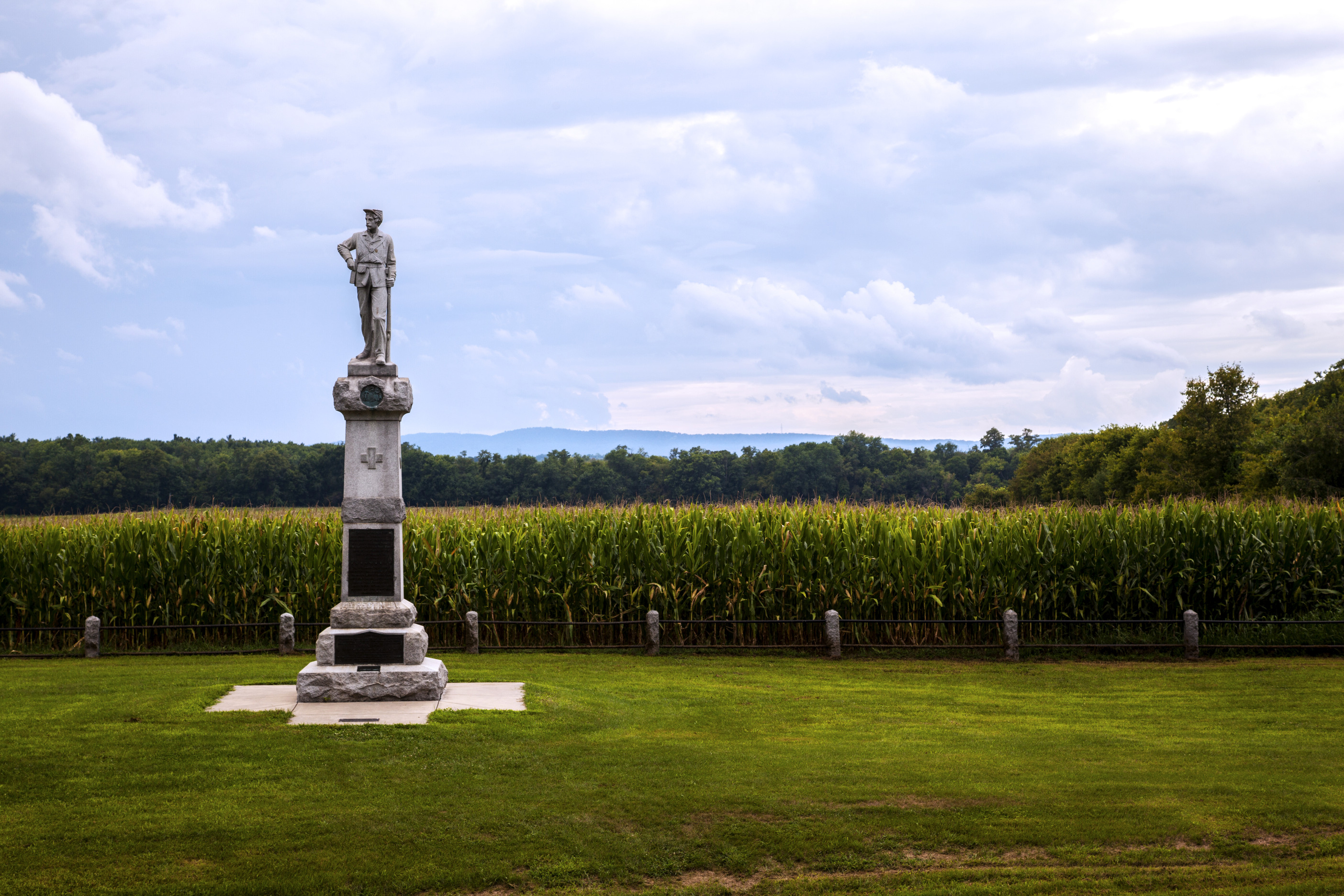A stone statue of a soldier in front of a farming field. 