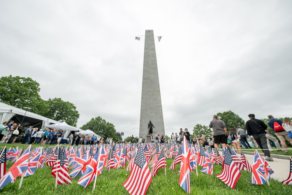 Rows of US and UK flags fill the lawn in front of the Warren Prescott Statue and Bunker Hill Monument