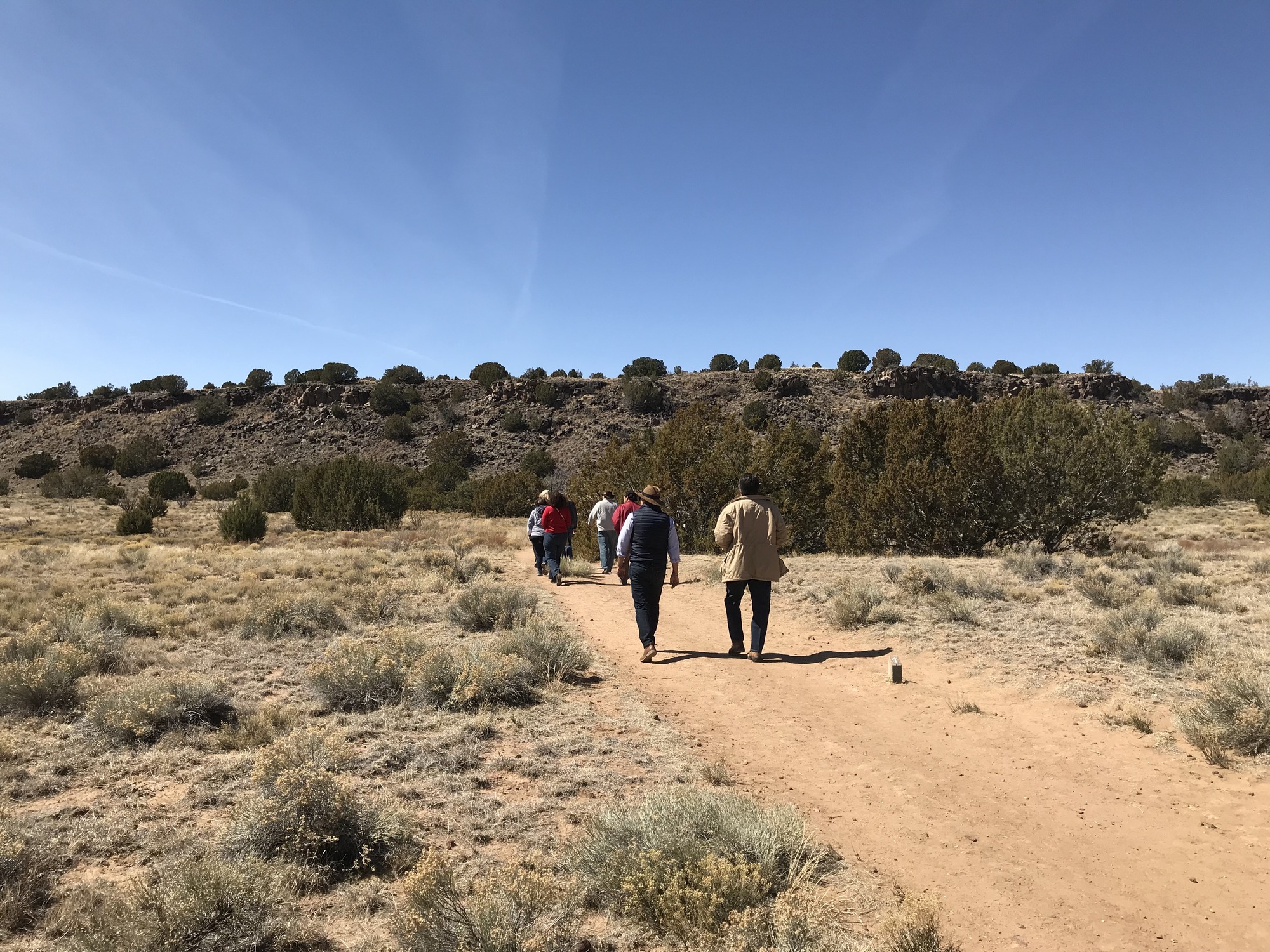 A group of people walking on a dirt trail in the desert.