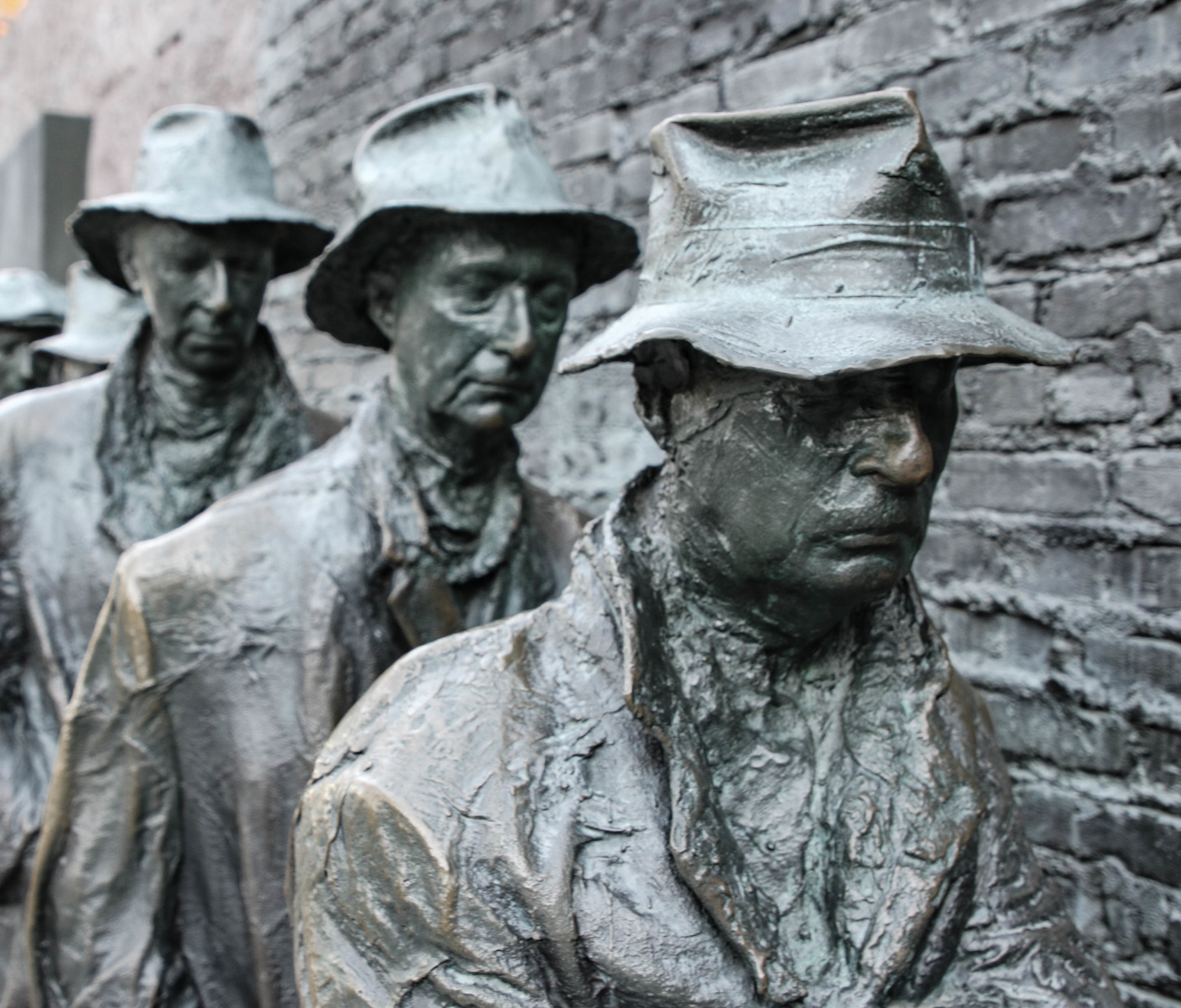 Statue of men standing in a line next to a brick wall
