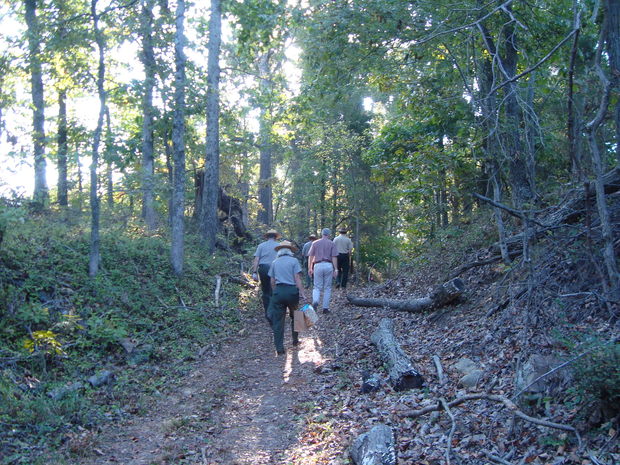 A group of people walking down a trail in the woods.
