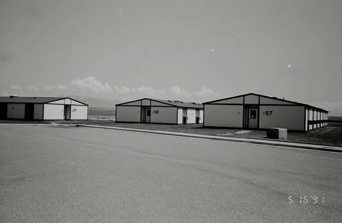 Barracks and parking area. Building numbers 57, 58, and 59. Mountains in background. [Image possibly for comparative housing study]