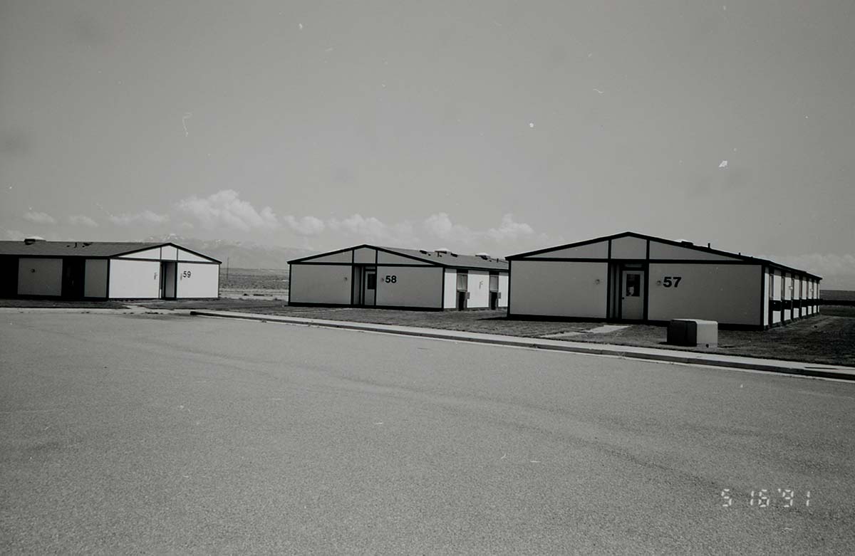 Barracks and parking area. Building numbers 57, 58, and 59. Mountains in background. [Image possibly for comparative housing study]