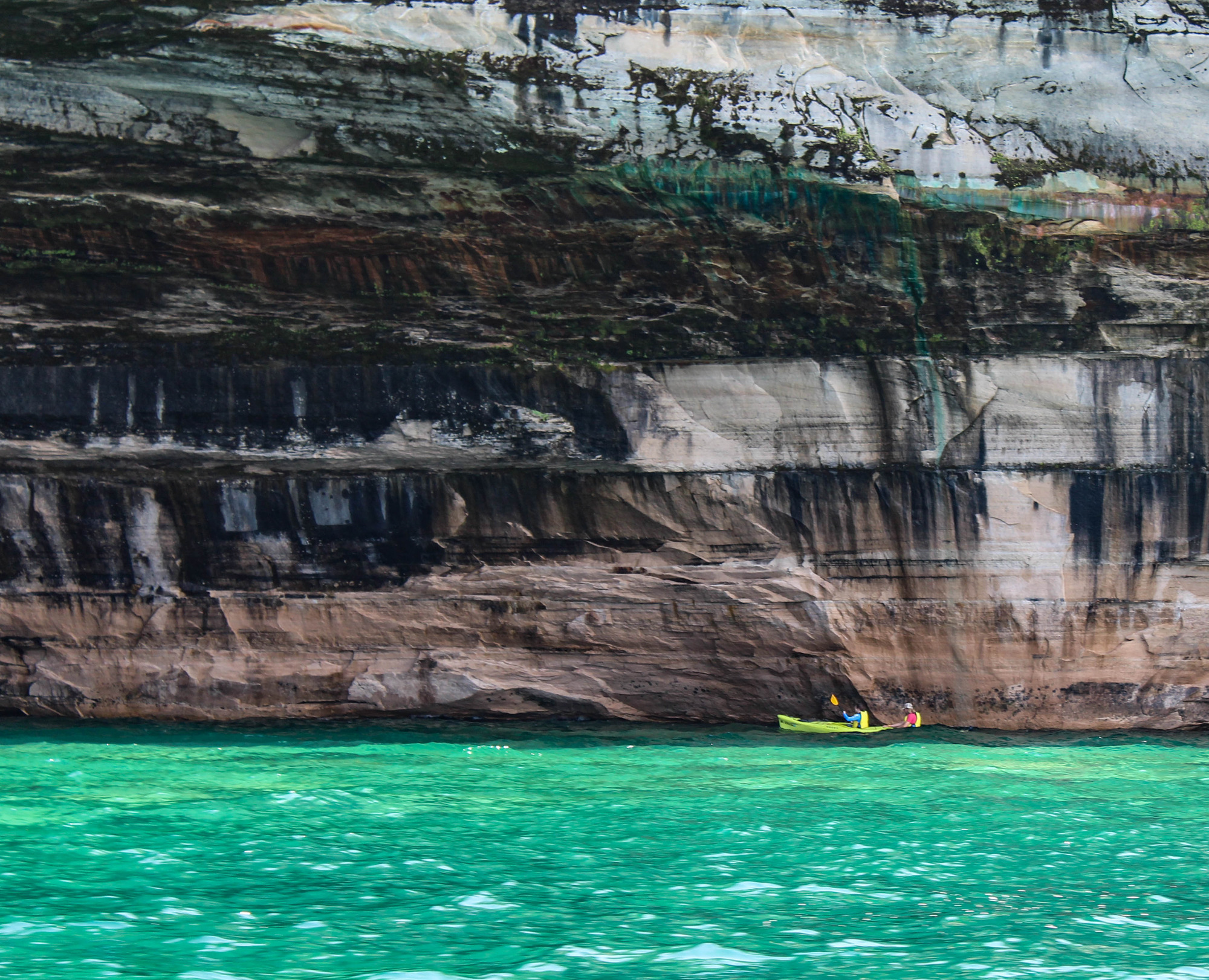 Kayakers by a tall rock wall along a lake