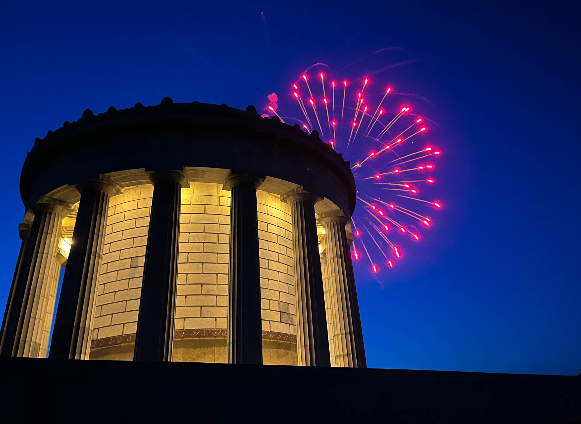 Nighttime fireworks over circular memorial building with prominent columns