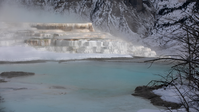 Looking across a hot pool of blue water at a steaming terrace formation.