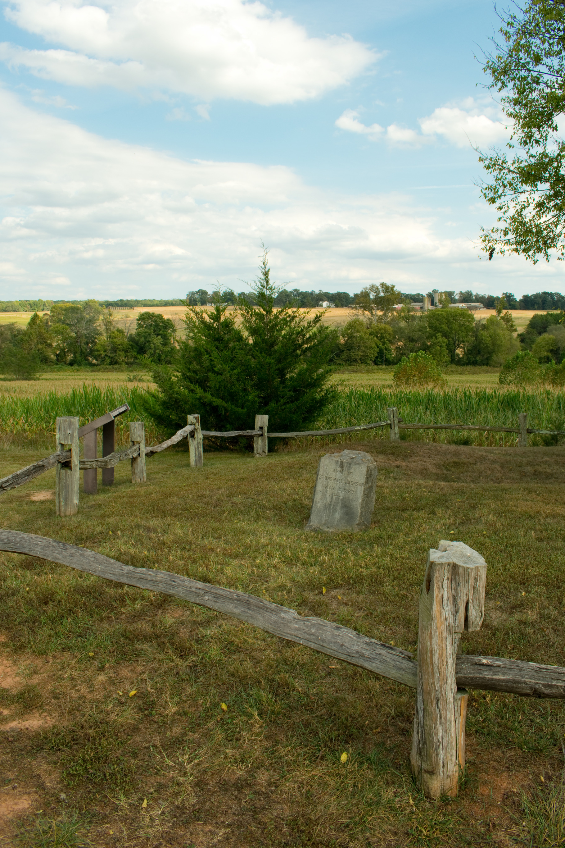 A gravestone surrounded by a wooden fence and fields. 