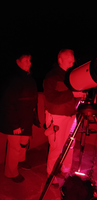 Two women with a telescope washed in red light at night.