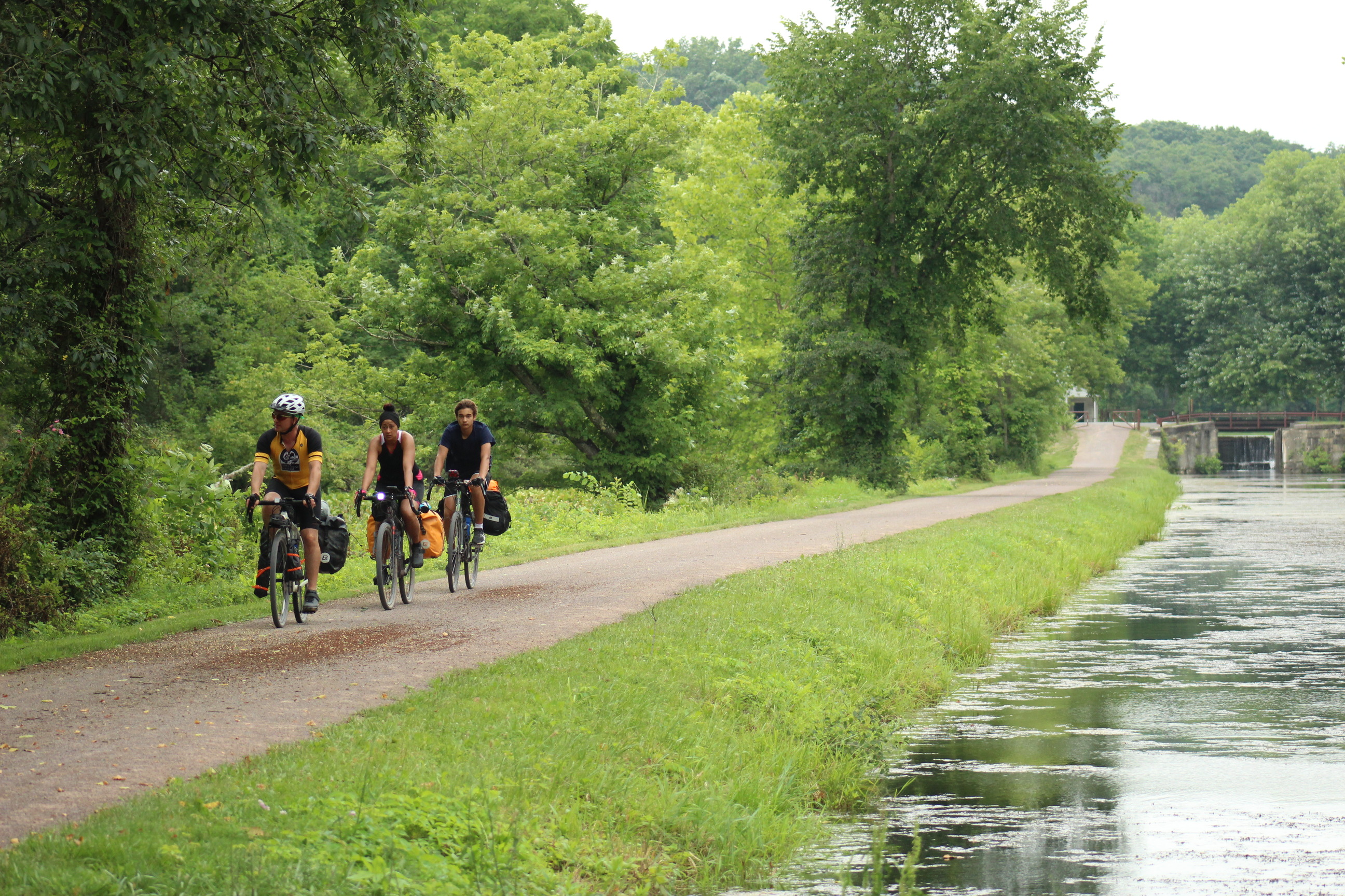 Three bikers riding on a path next to a canal.
