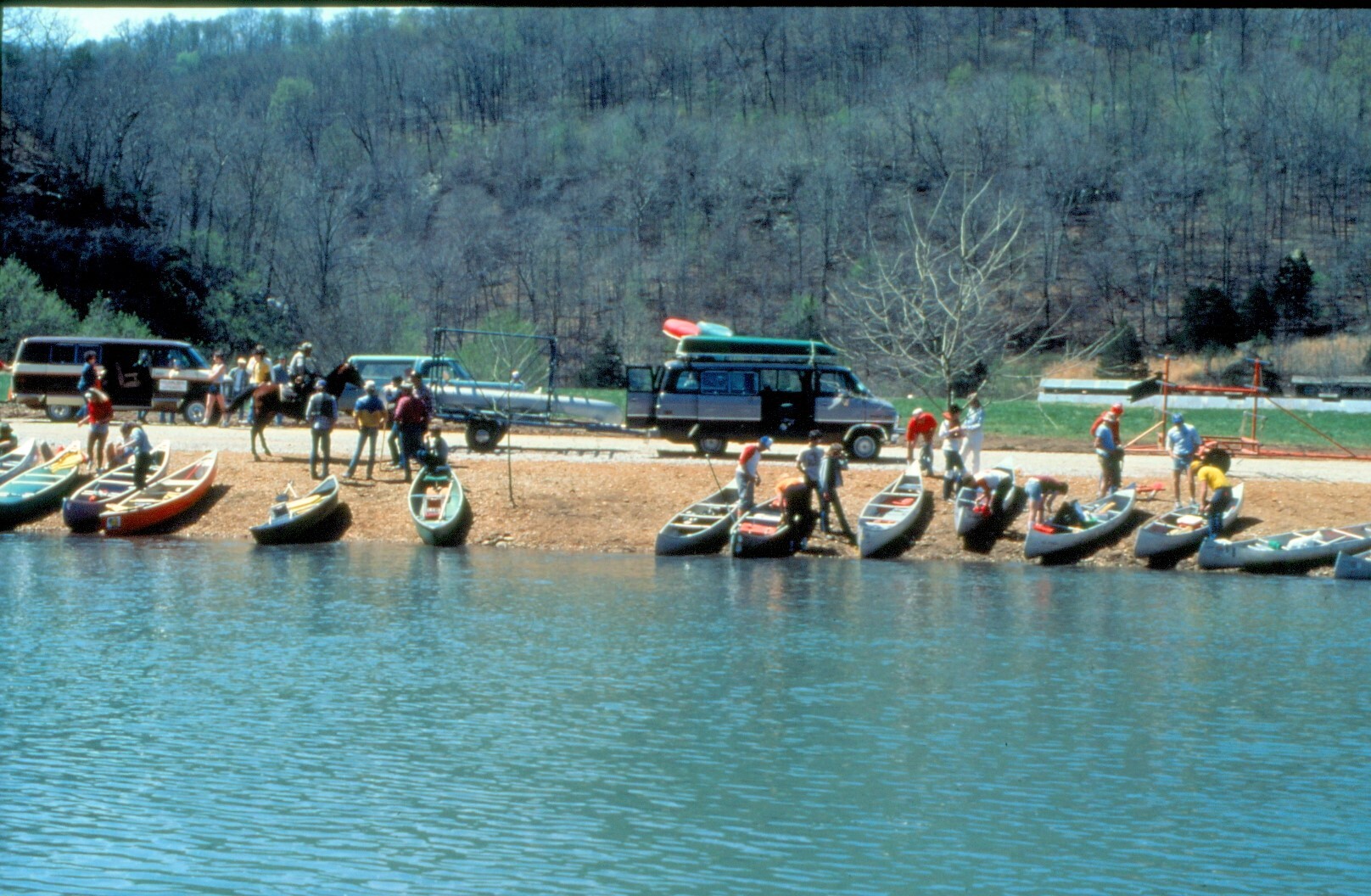 color photo with river in foreground and boats and people in center on river bank.