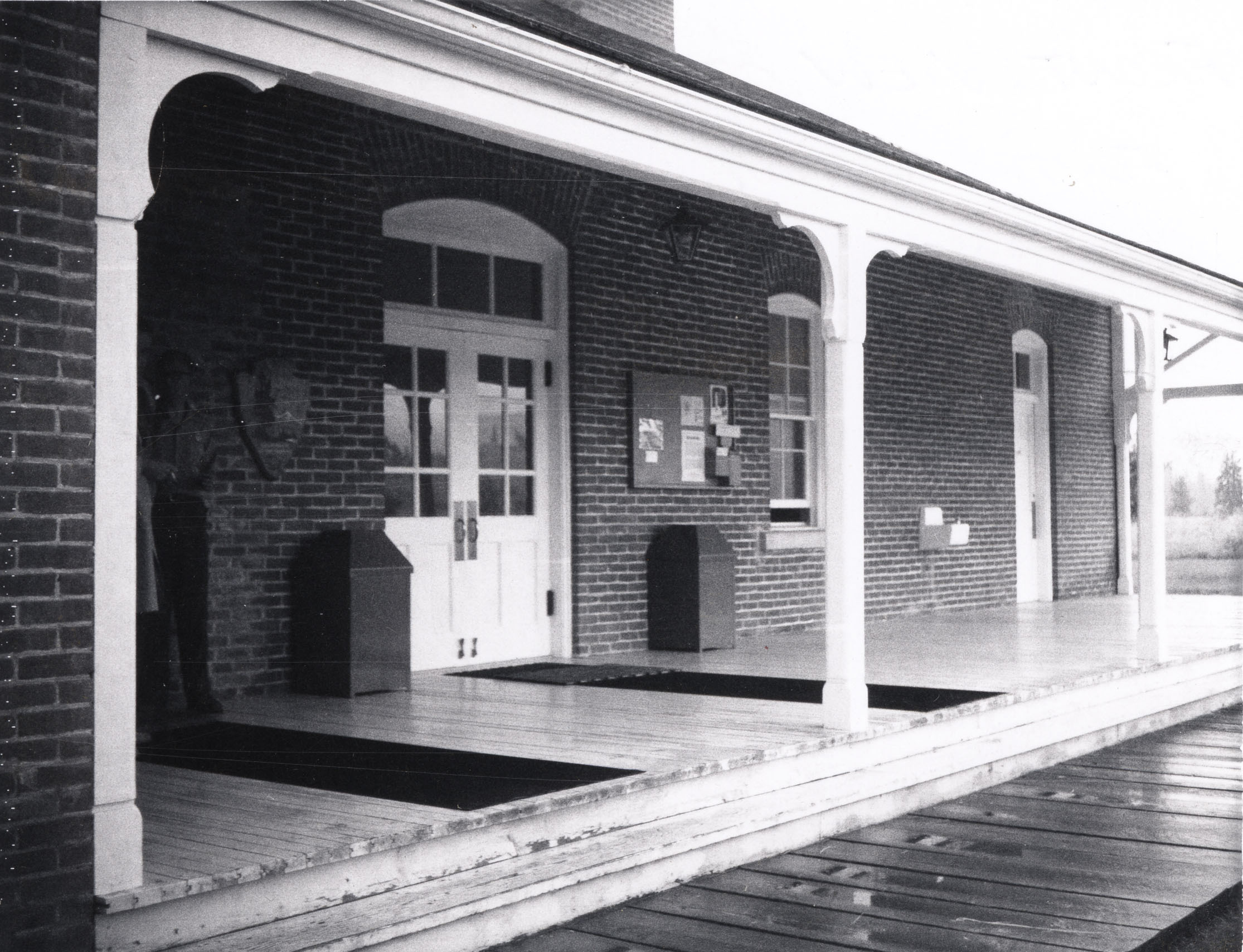 Black and white photo of the front porch of a brick building. 