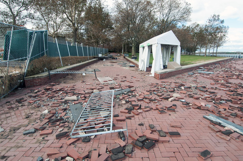 A redbrick walkway with a section of metal fence laying on the ground surrounded by debris.