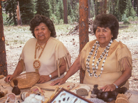 Two women stand in front of a display of Atsugewi crafts.