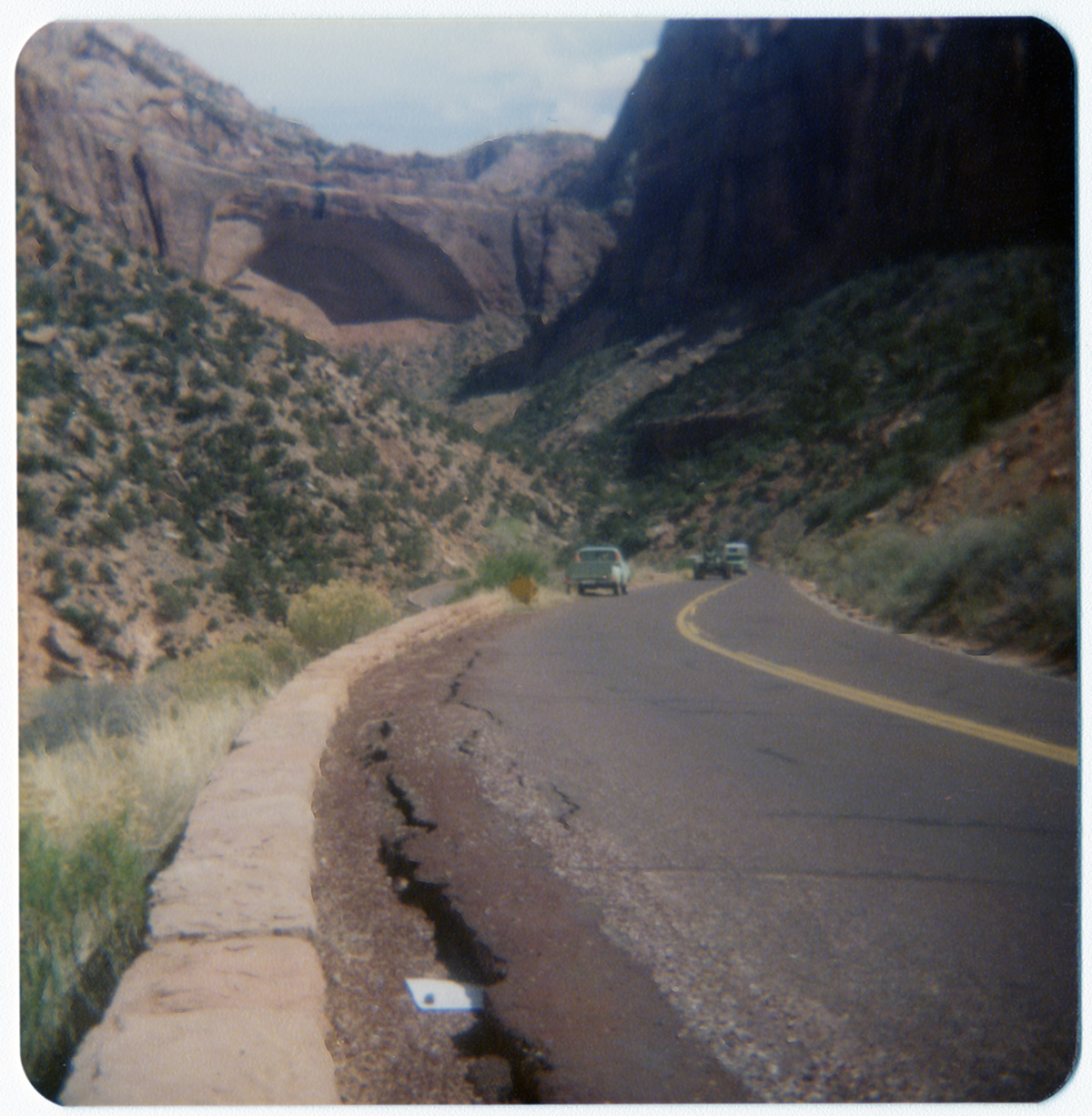 Crack in road in need of repair with paper marking over top, with Zion landscape in background.