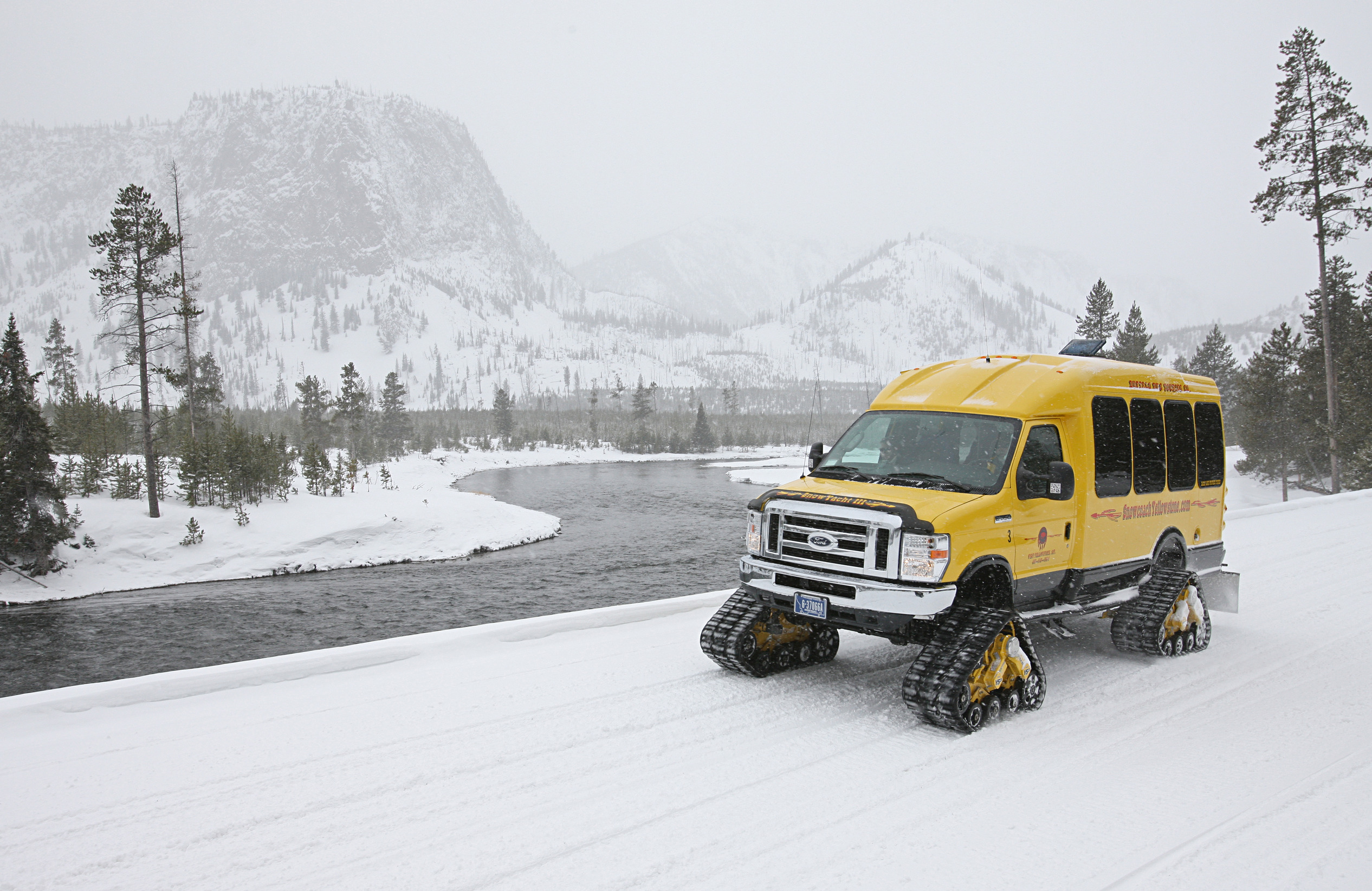 Yellow snowcoach  driving on snow packed road alongside the Madison River