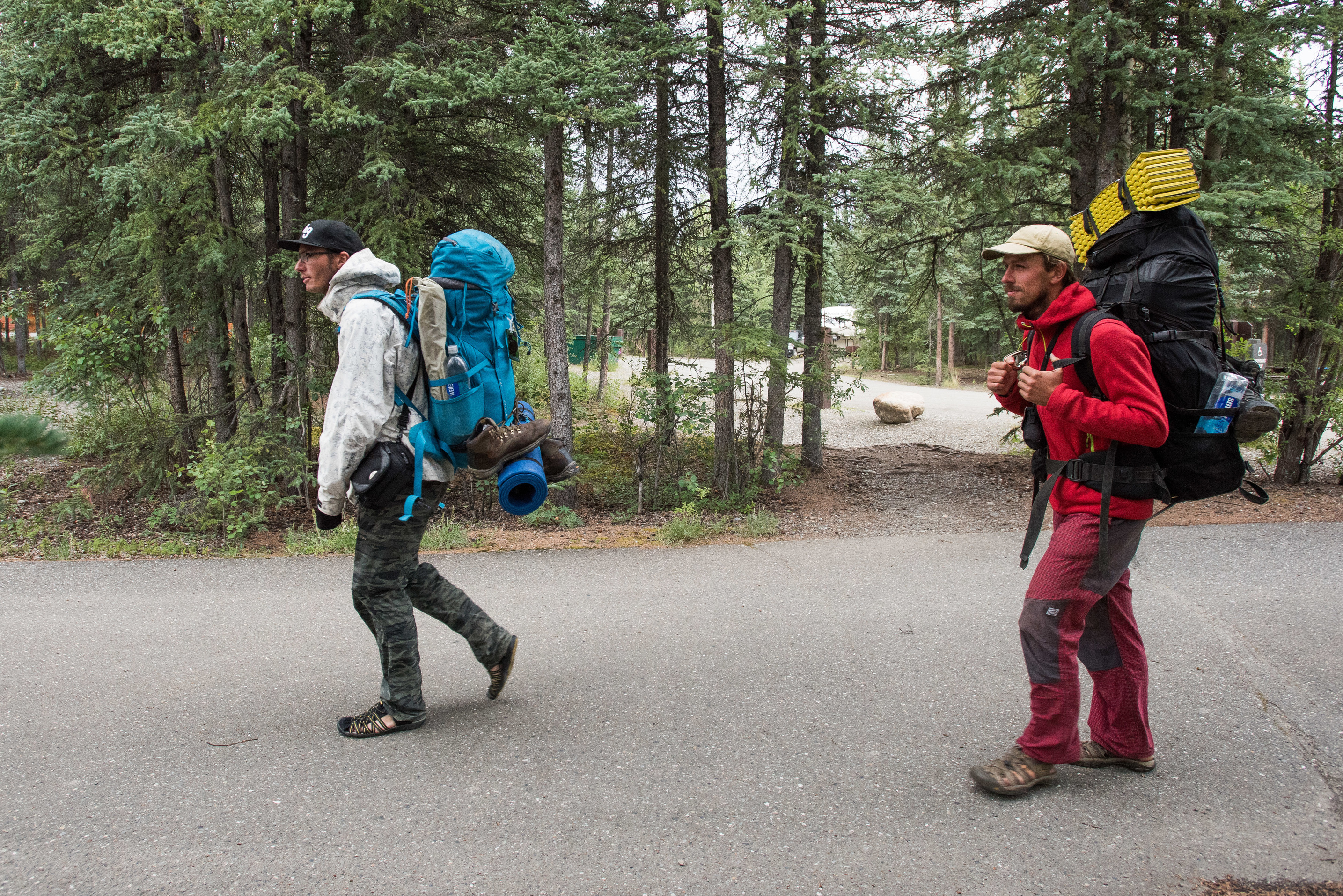 two men with backpacks walking on a campground road
