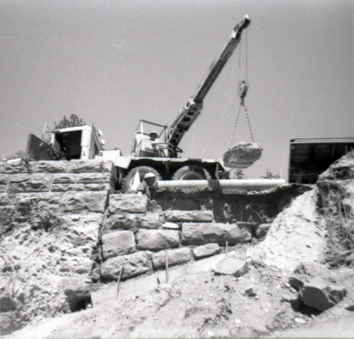 Man operating a crane lifting a rock during the retaining wall repairs along the East Rim road.