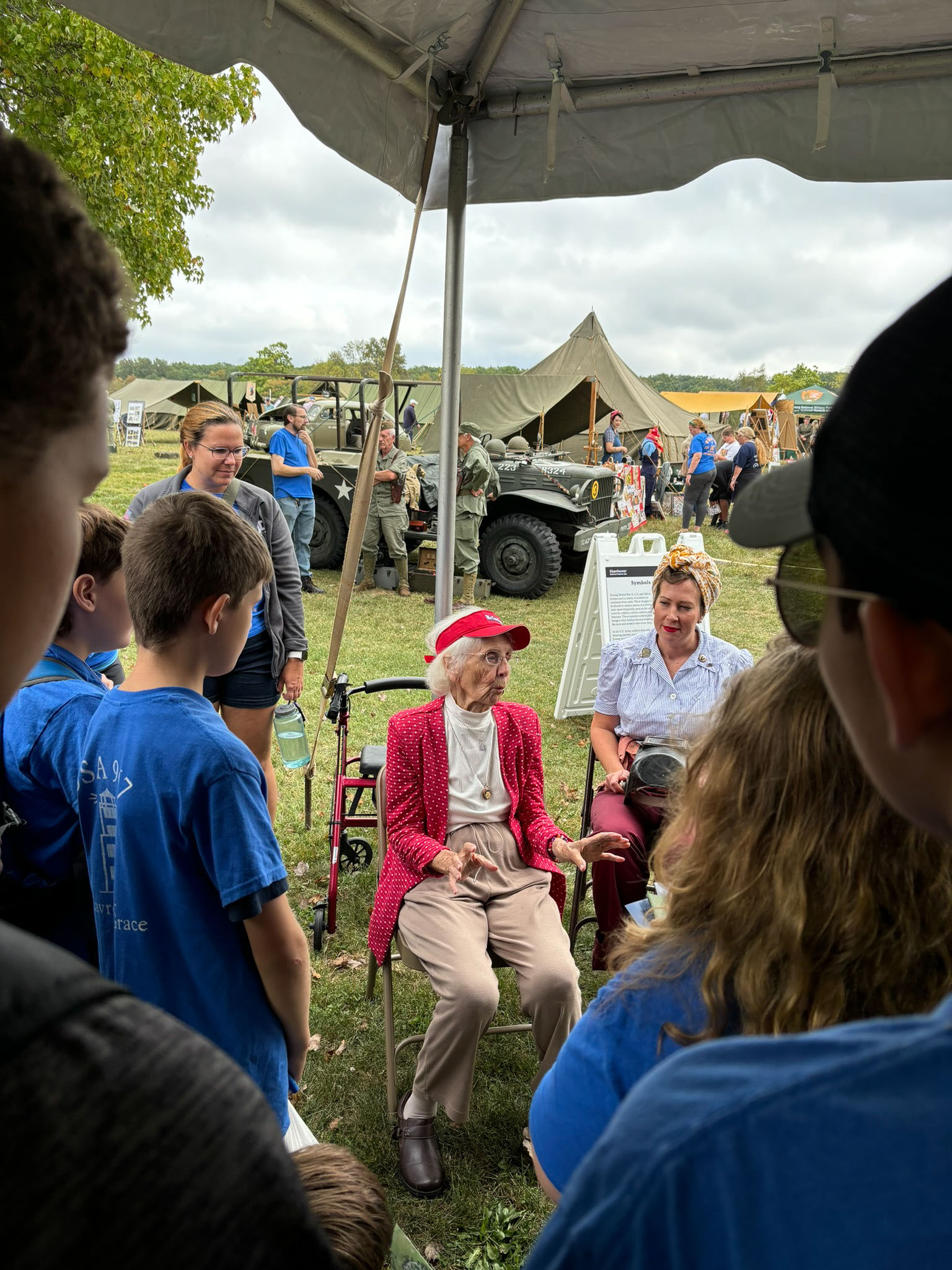 Two women sit while a group stands and listens. 