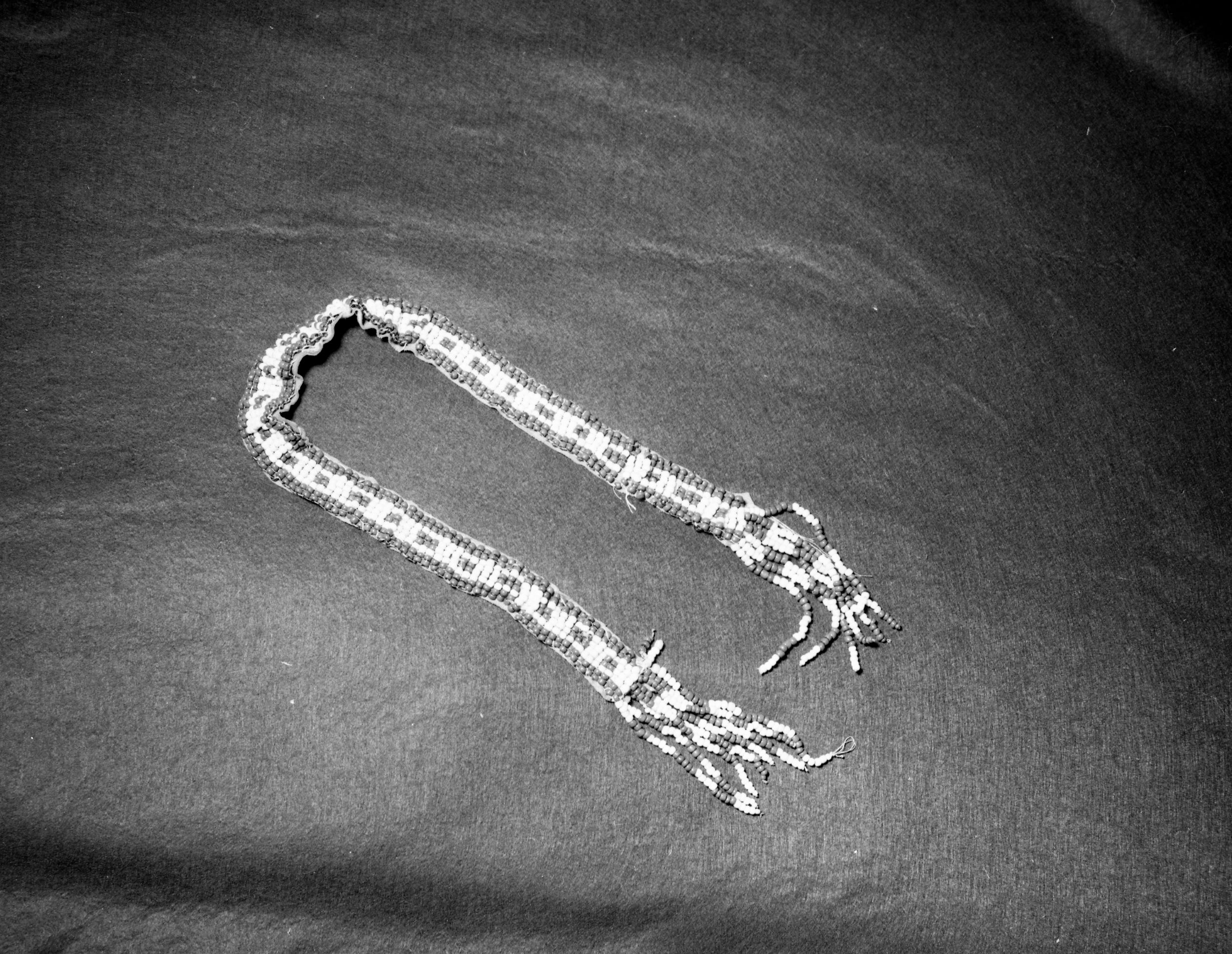 Mrs. Geraldine McConnell Collection. Object: Miwok beaded belt. Dimensions: Beaded sectoin - 26 1/2" x 2 1/4" with a 4 1/4" fringe on each end. Materials: Commercial thread, opaque white glass paste and green centered brick red exterior cornaline d'alleppo beads. Technology: Single thread loomwork. Collection History: Dates from perhaps the middle of the last century. Made by a Miwok woman from the American Camp that was married to an English trader and was the grandmother of Mary Plummer. Photographed by Michael Dixon in January 1983. Catalogued by Craig Bates and Barbara Beroza. Yosemite Collections, National Park Service.