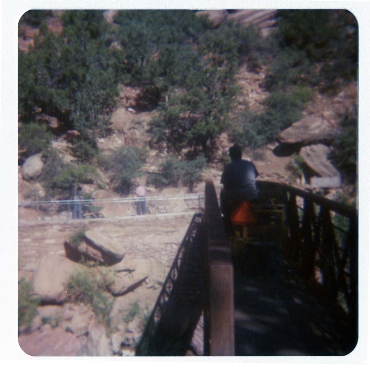 Man driving sweeper equipment across the new Grotto footbridge after its placement on stone abutments. Men working on trail in background.