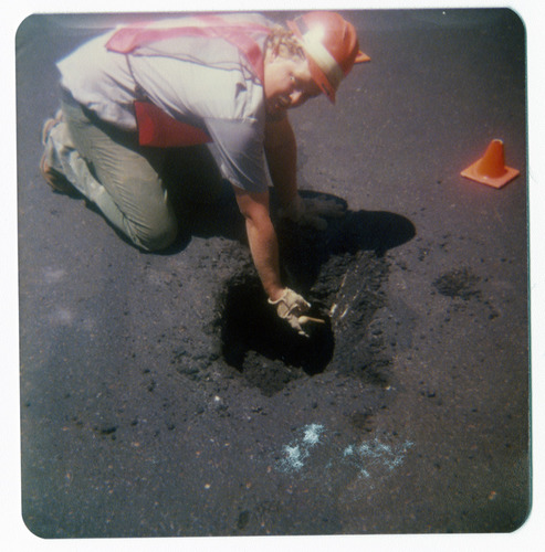 Man working on repairing pot hole in road.