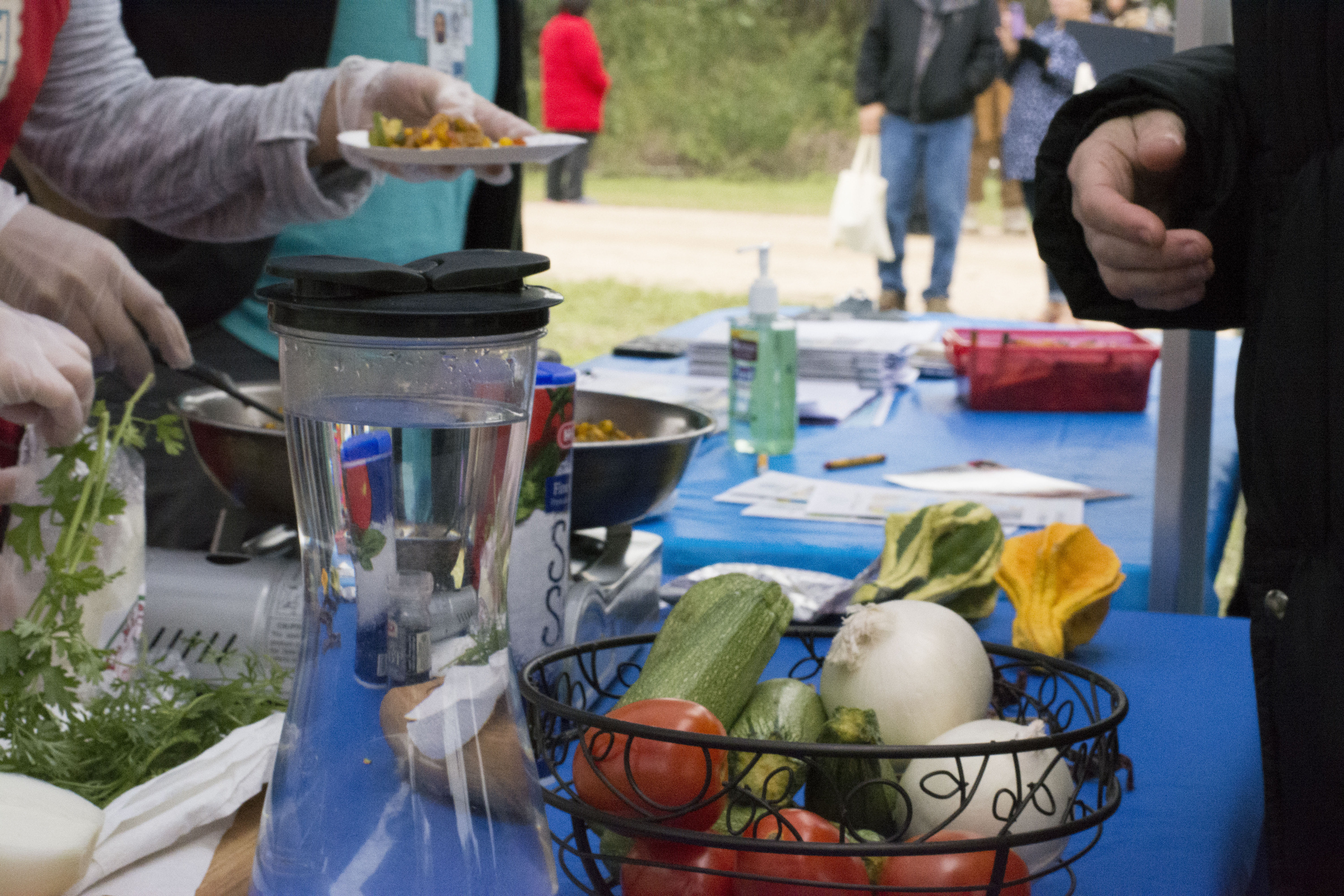 Table with water, and fresh produce such as tomato, onion, and zucchini. 