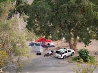 looking down at two camp tents, SUV and motorcycle in shade of large tree